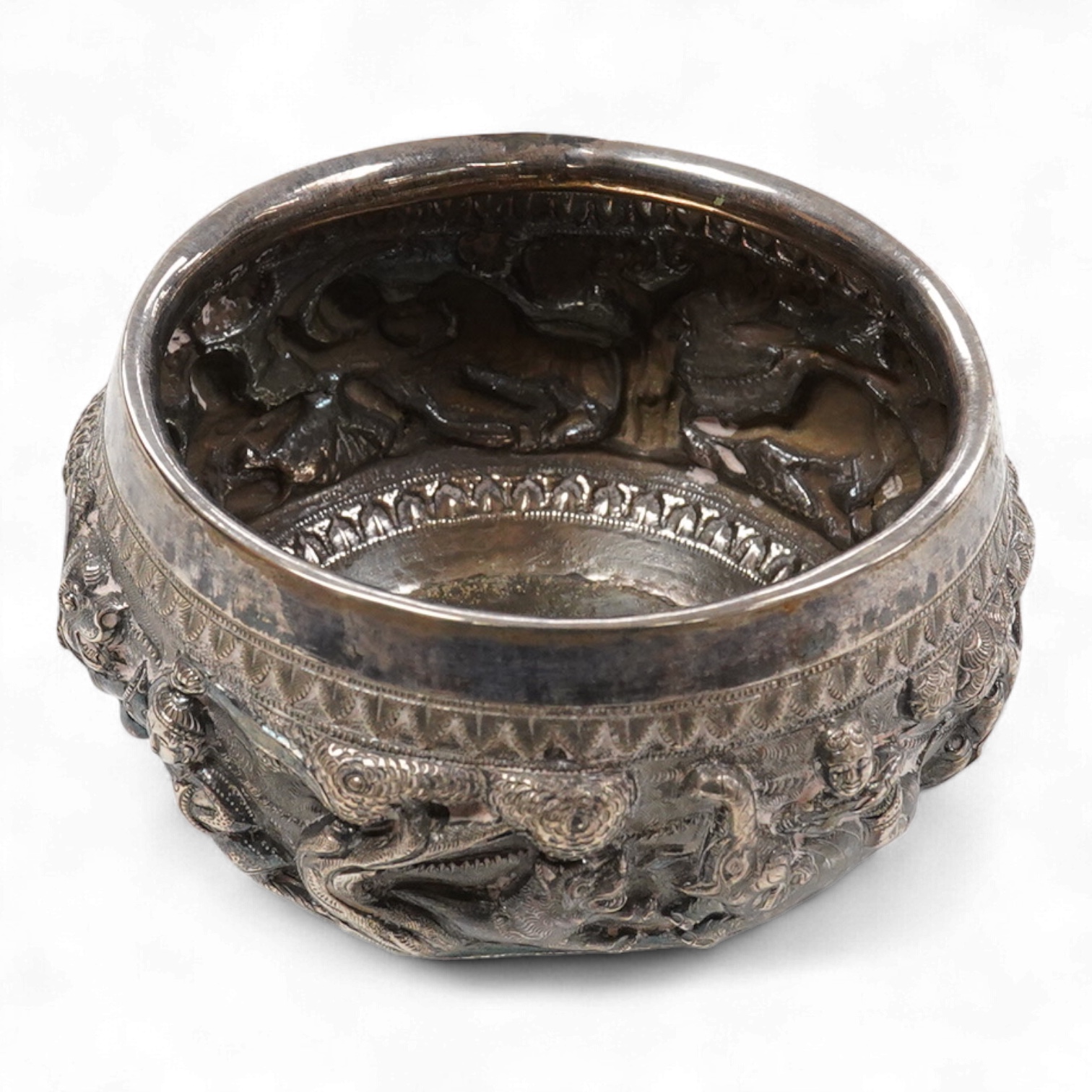 A late 19th/early 20th century Burmese white metal bowl, embossed with figures and animals in continuous battle scene, top diameter 12.4cm.